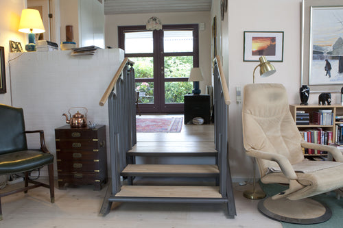 Liftup FlexStep in staircase mode in a home: three pale wood treads in a grey frame with wooden handrails, rising to a garden door at the upper floor