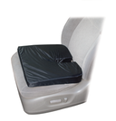 Black coccyx orthopedic seat cushion with U-shaped cutout placed on the driver's seat of a car, positioned over a light gray seat cover, demonstrating in-use placement with the cutout oriented toward the back for tailbone relief.