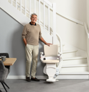 Man standing next to the Otolift Modul-Air Smart at the bottom of a curved staircase, showing the slim single rail following the inside of the curve.