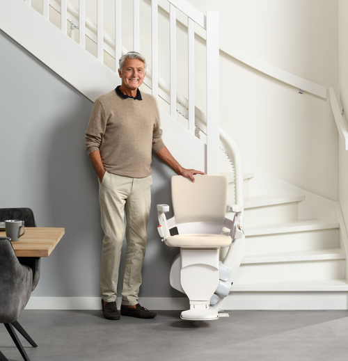 Man standing next to the Otolift Modul-Air Smart at the bottom of a curved staircase, showing the slim single rail following the inside of the curve.
