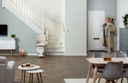 Living room view of the Otolift Modul-Air Smart parked on its slim rail at a curved staircase, seat folded down.