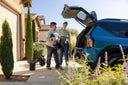 Two people carrying Strutt ev¹ modules to the open tailgate of an SUV, with more modules on the driveway
