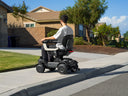 Rider on a Strutt ev¹ driving along a residential sidewalk, seen from the side and behind