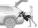 A woman lifting the folded WHILL Model C Lite into the open rear cargo area of a white SUV.