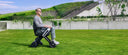 A man seated in the WHILL Model C Lite driving across a grass lawn in a landscaped park.