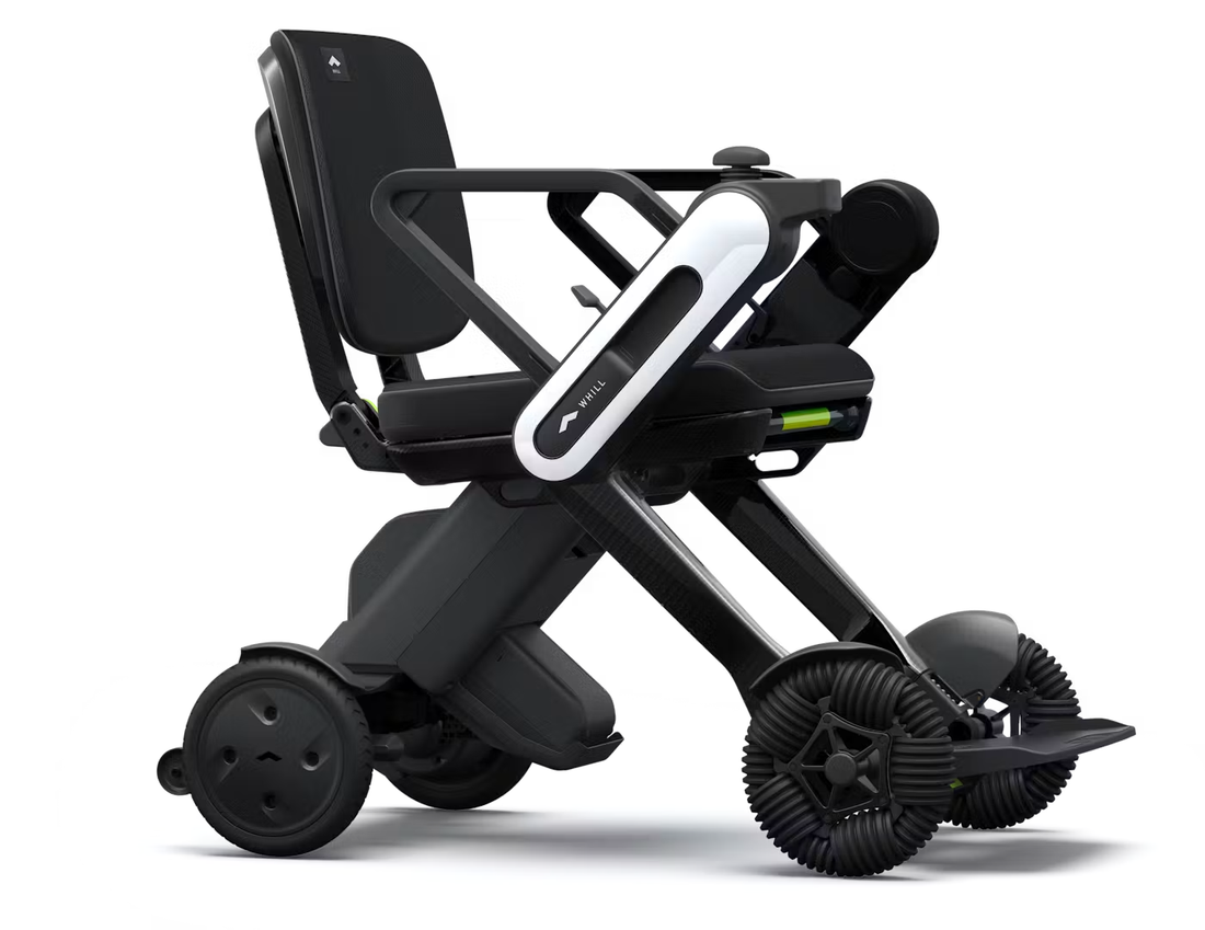 WHILL Model C Lite folding carbon electric wheelchair, side view, showing the carbon fibre X-frame, black seat and backrest, white WHILL arm-mounted controller, and front omni-directional wheels.