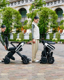 Two photos side by side: a woman folding the WHILL Model C Lite by its backrest on a paved plaza, then standing beside the folded chair.
